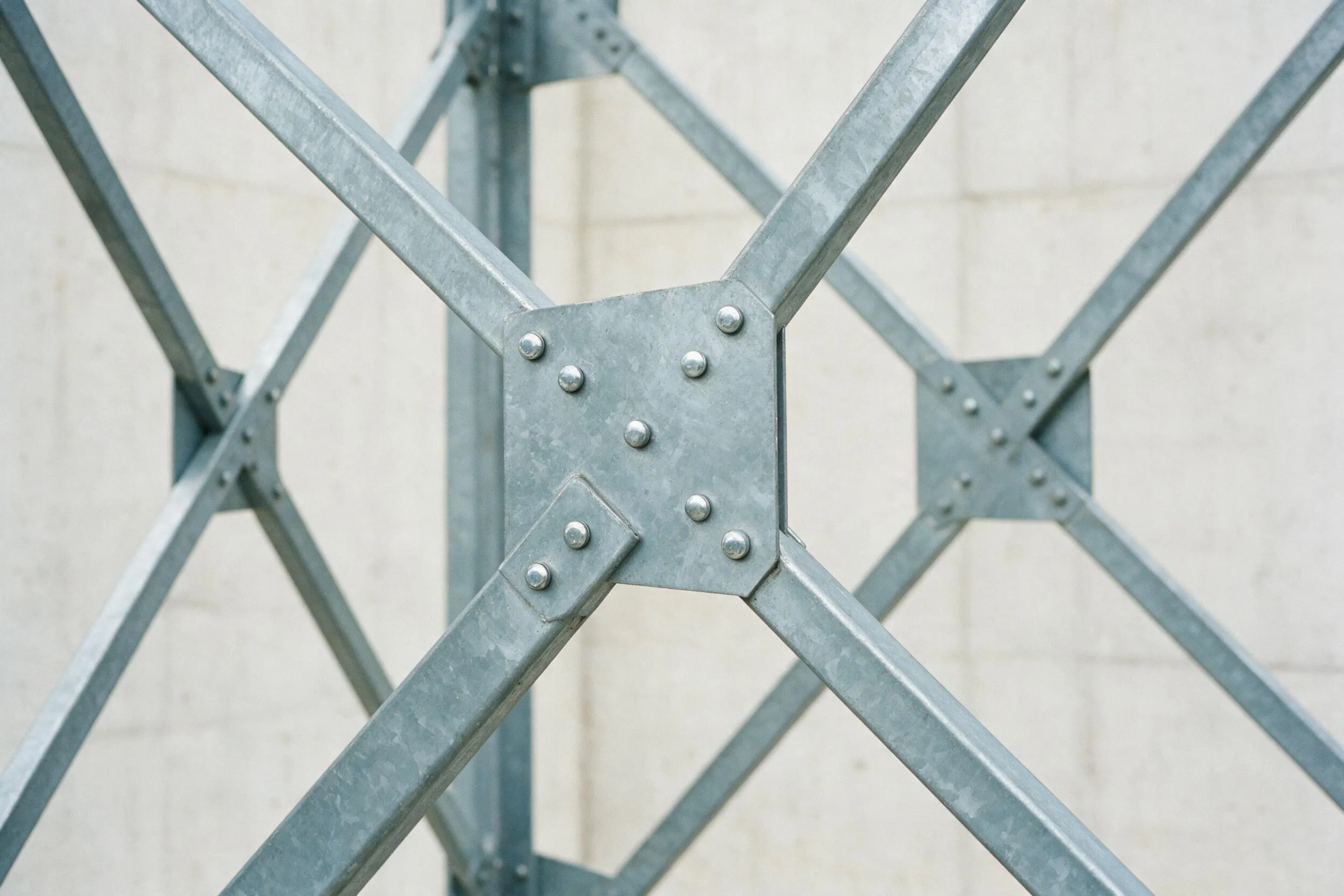 Galvanized steel cross-bracing bolted to a pale concrete wall, symmetrical connection plate in focus