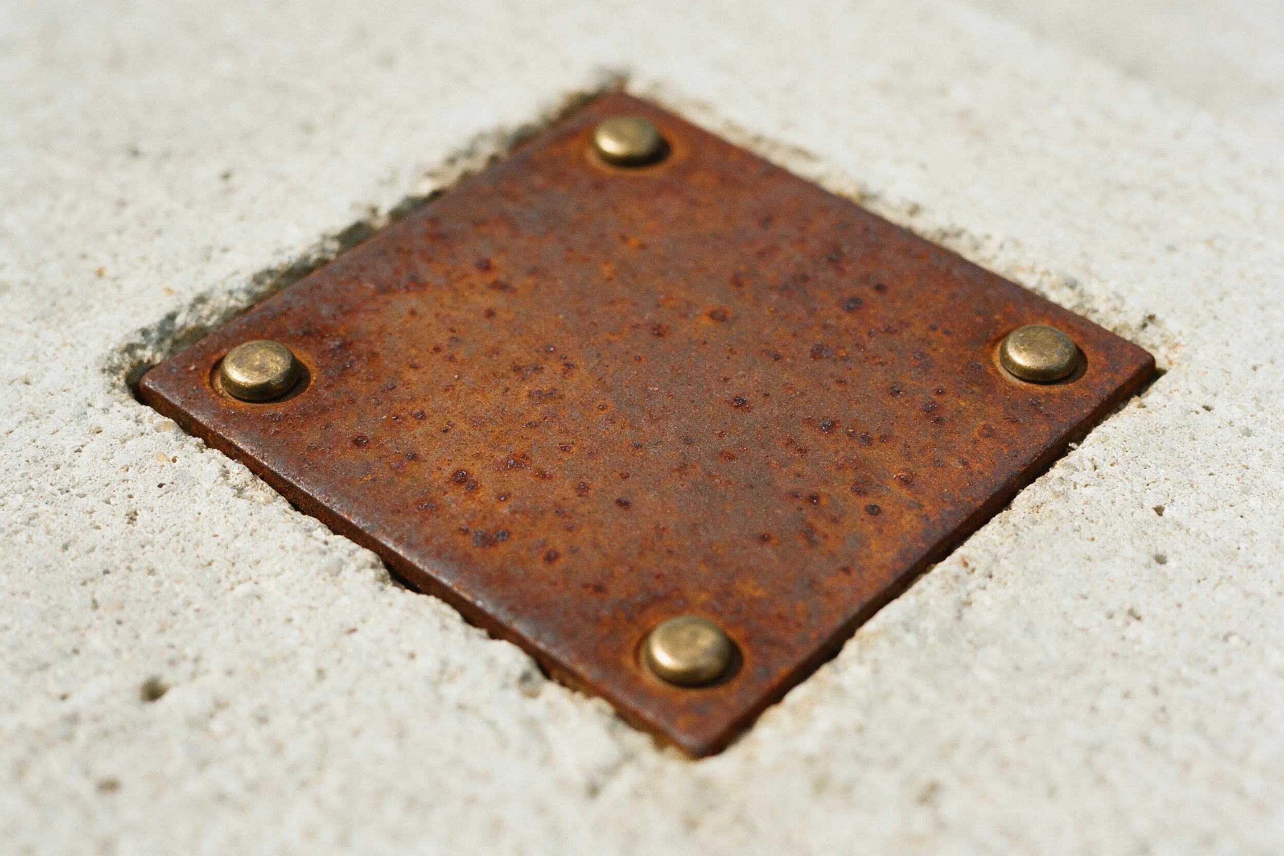 Weathered corten steel plate with brass bolts set flush into pale concrete